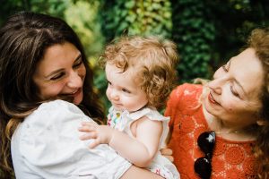 Italian Family Photographer featuring three generations of women. A Mum and Grandma surround their 9-month old daughter/grand-daughter. They're all laughing.
