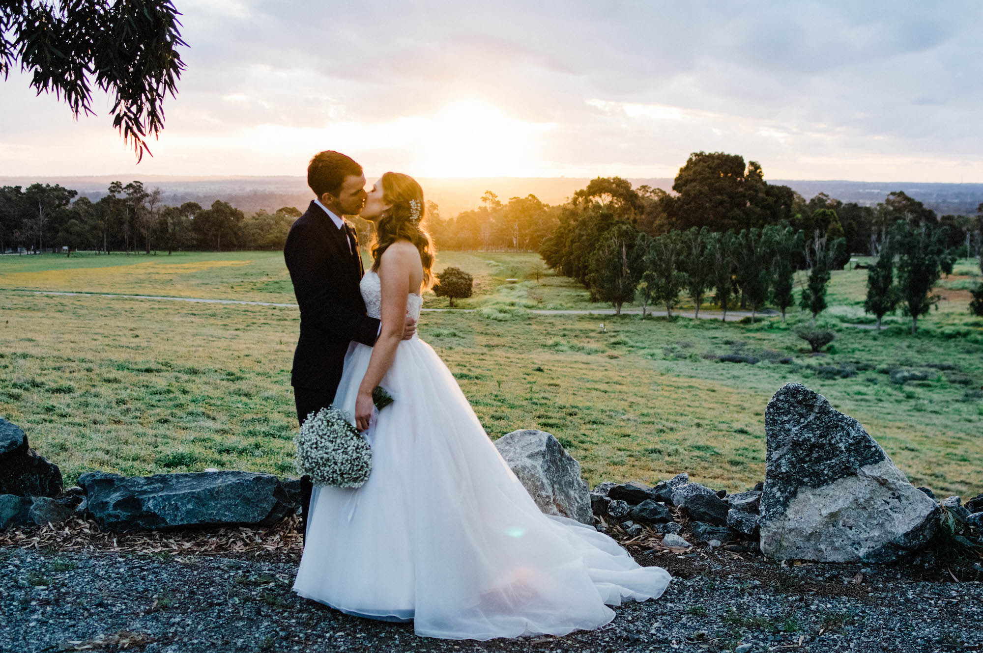 The bride & groom share a kiss in front of the sunset, taken by a perth wedding photographer.