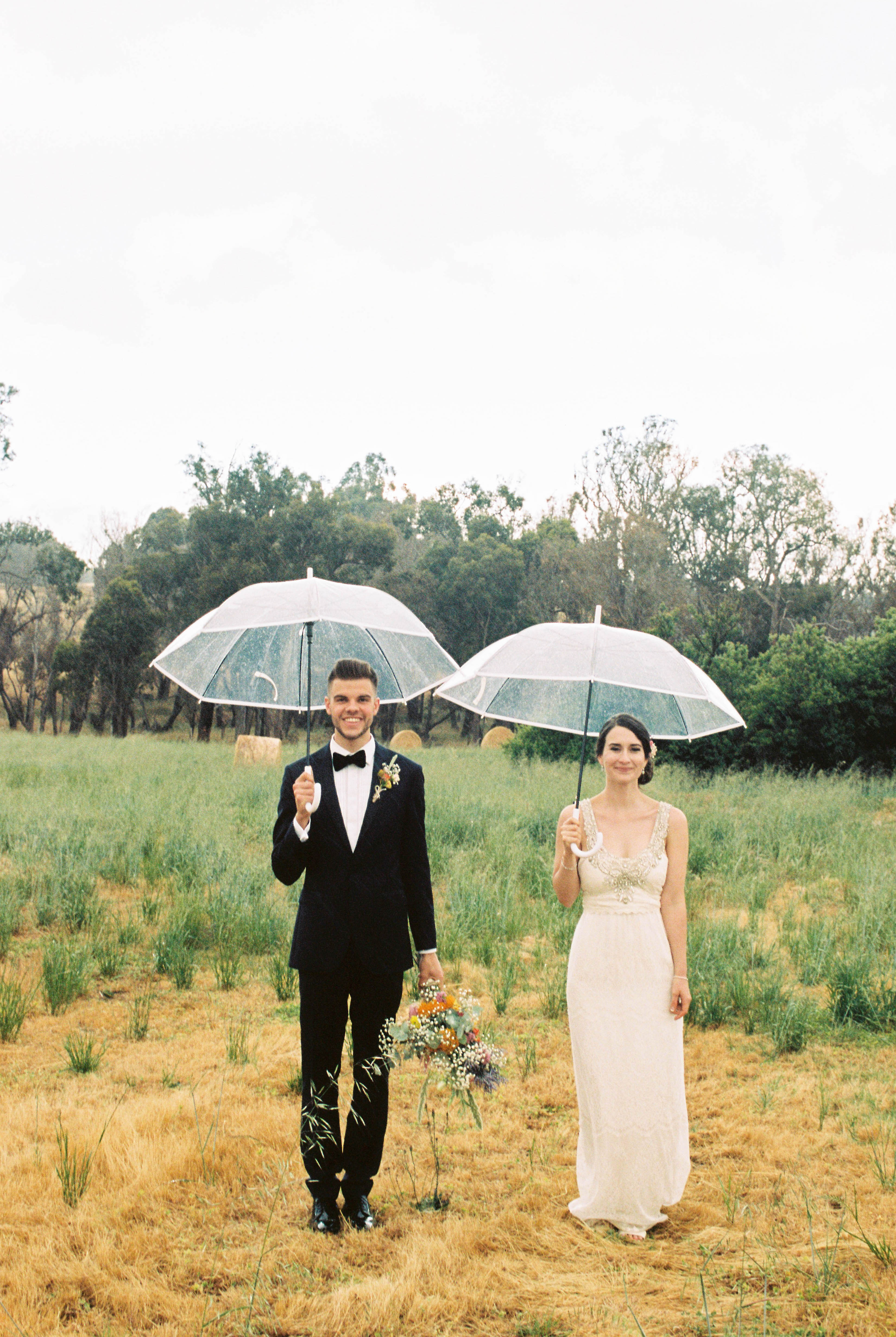 A wedding portrait of the bride & groom standing side-by-side in the rain on their family farm