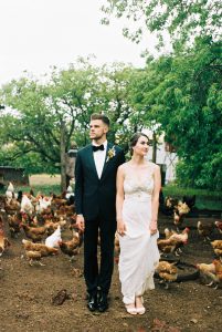 Wedding photography of the bride & groom posing in a chicken pen on their family farm