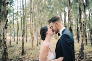 Natural wedding portraits of the bride and groom kissing in a blue gum plantation