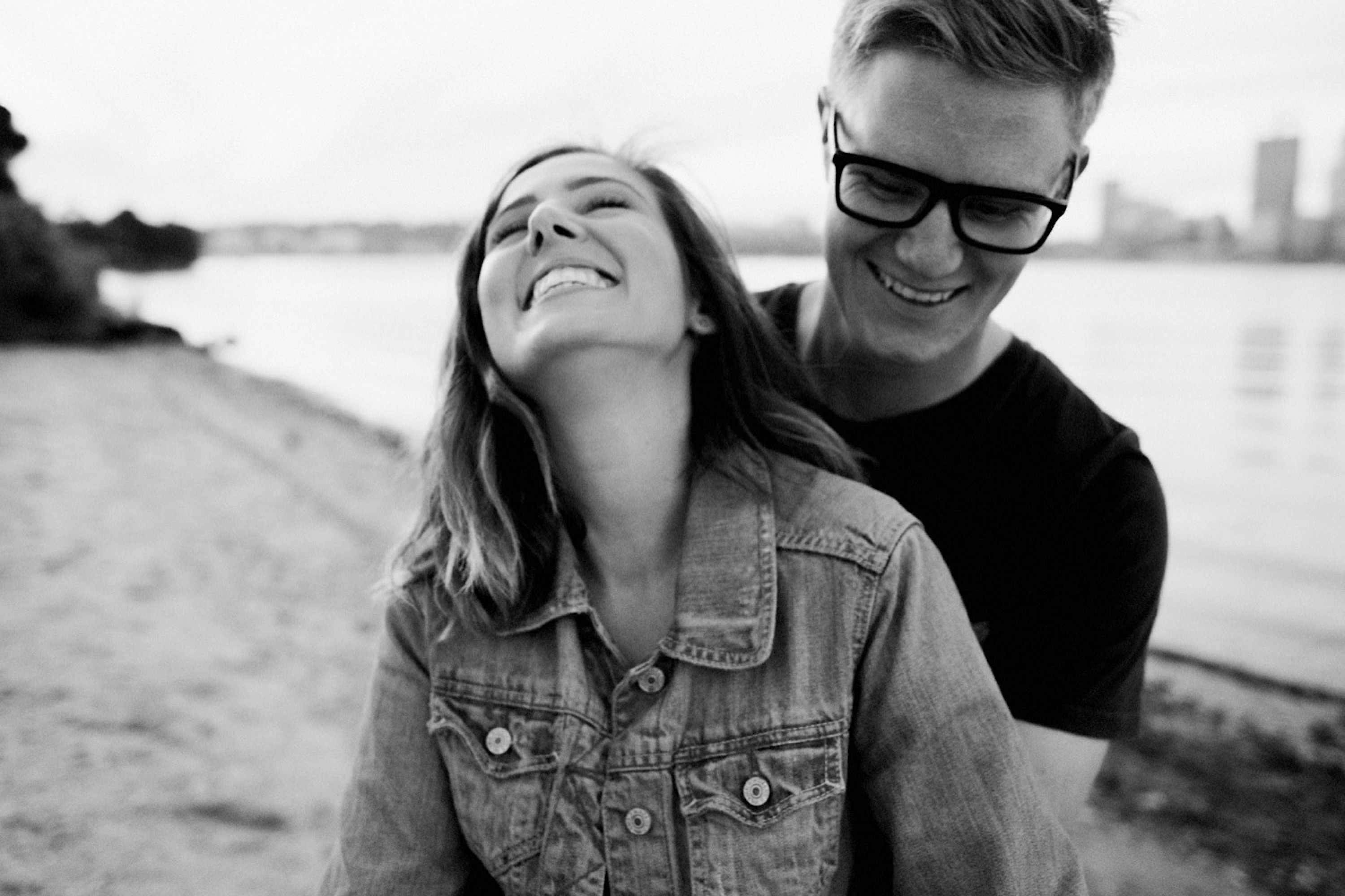 A black & white couple portrait of a young couple laughing on the beach.