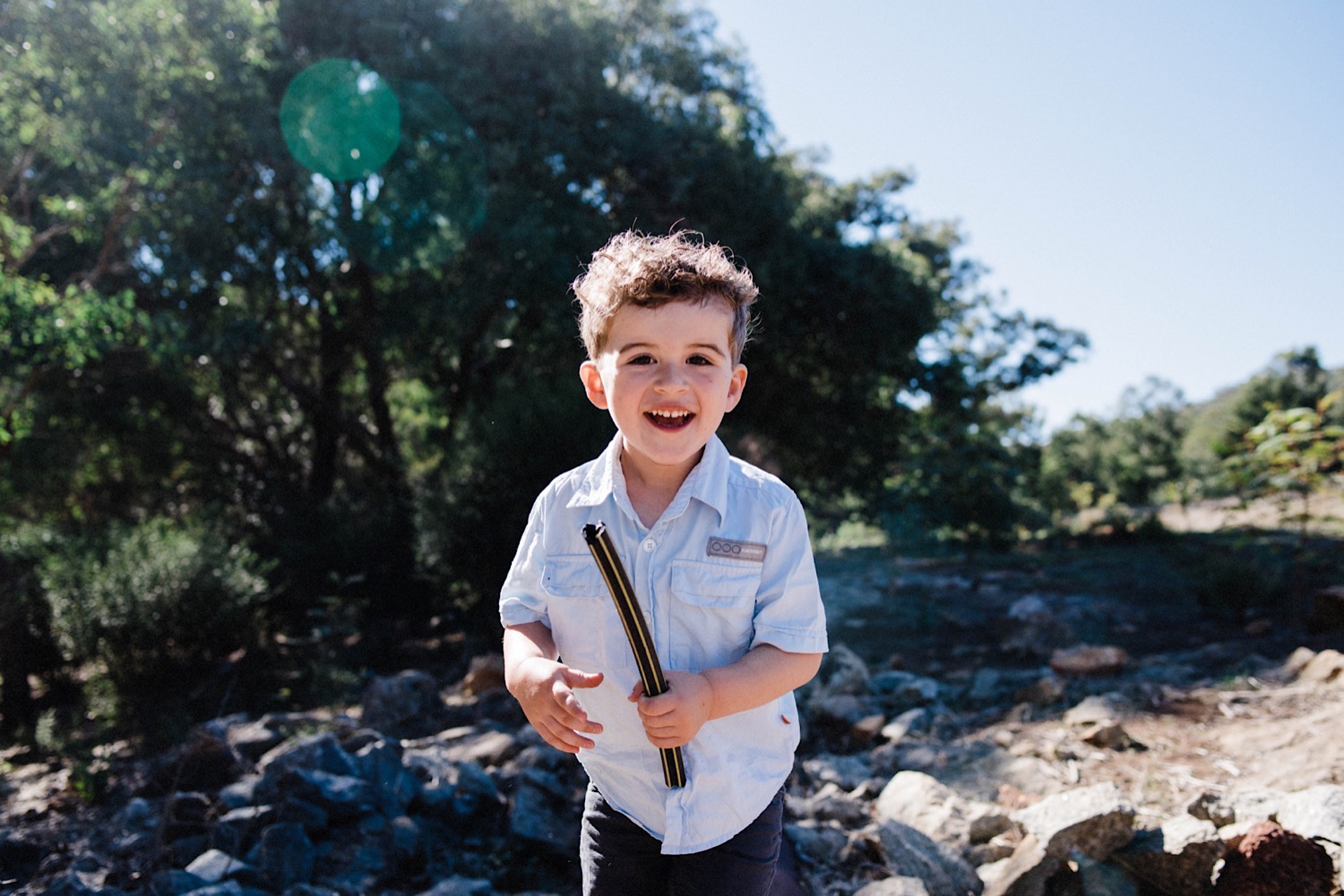 A candid, Lifestyle Family Portrait of a little boy smiling at the camera with a stick he found during their hike in Roleysotne.