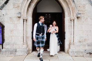 A candid portrait of the bride & groom walking out of St John's Anglican Church at the end of the wedding, as their bride hold's a friend's baby.