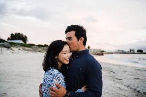 A couple hug while standing at Bathers Beach during their Fremantle Engagement Portrait session.
