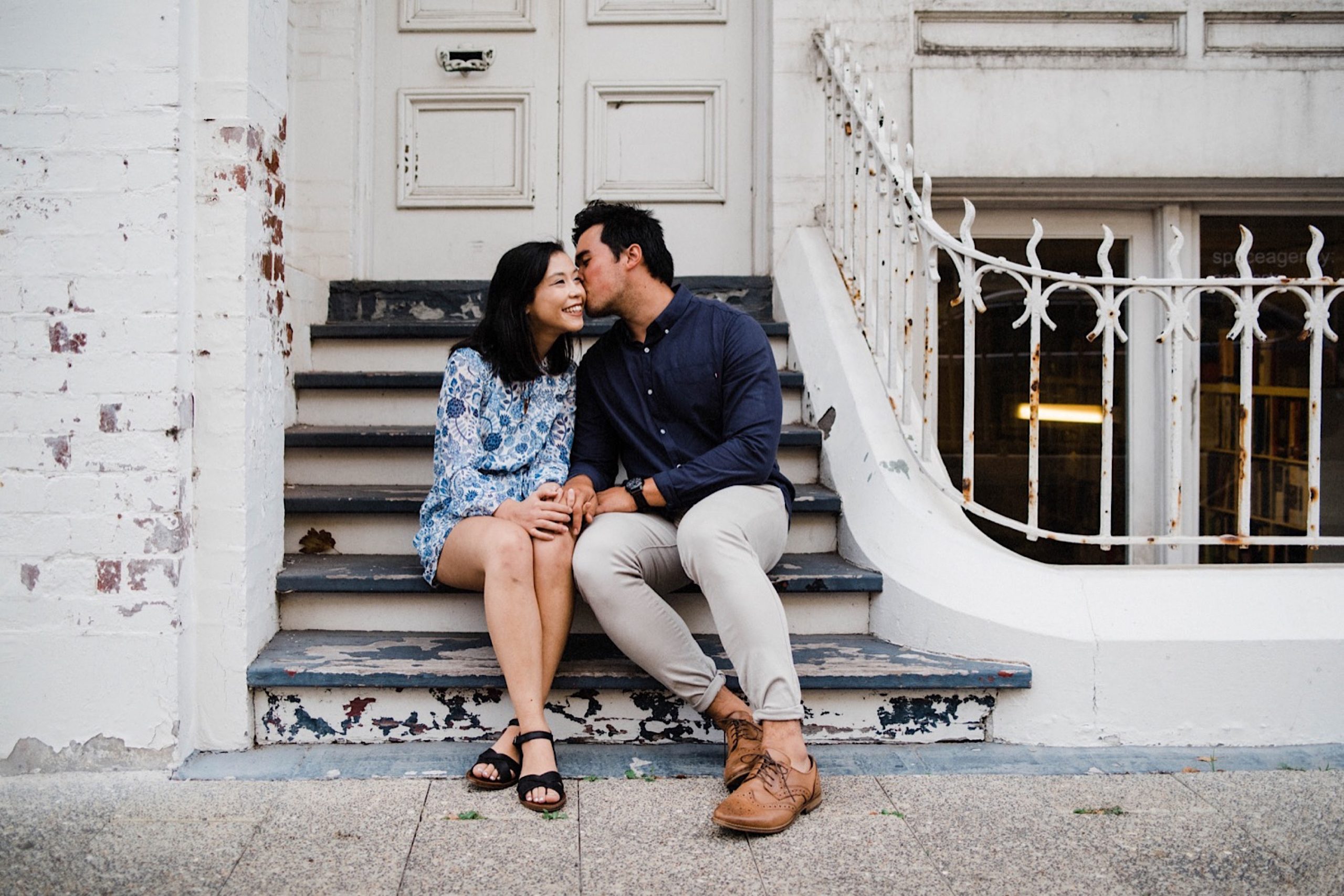 Romantic Fremantle Engagement Photography of a couple wearing blue and sitting in front of an old, white & green building.