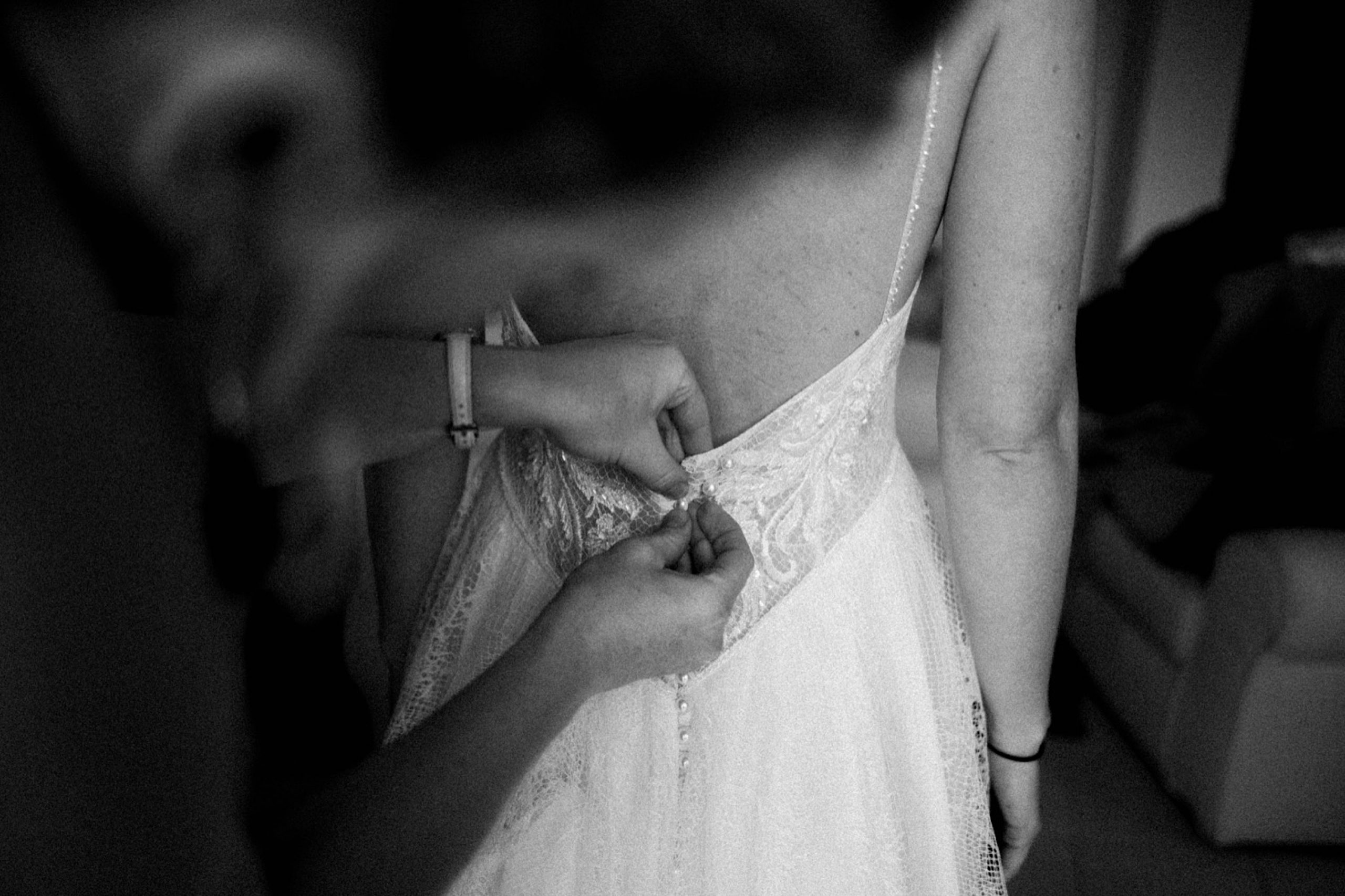 A black & white wedding photo of a bride's Mum helping her to button up her Flora Bridal Dress.