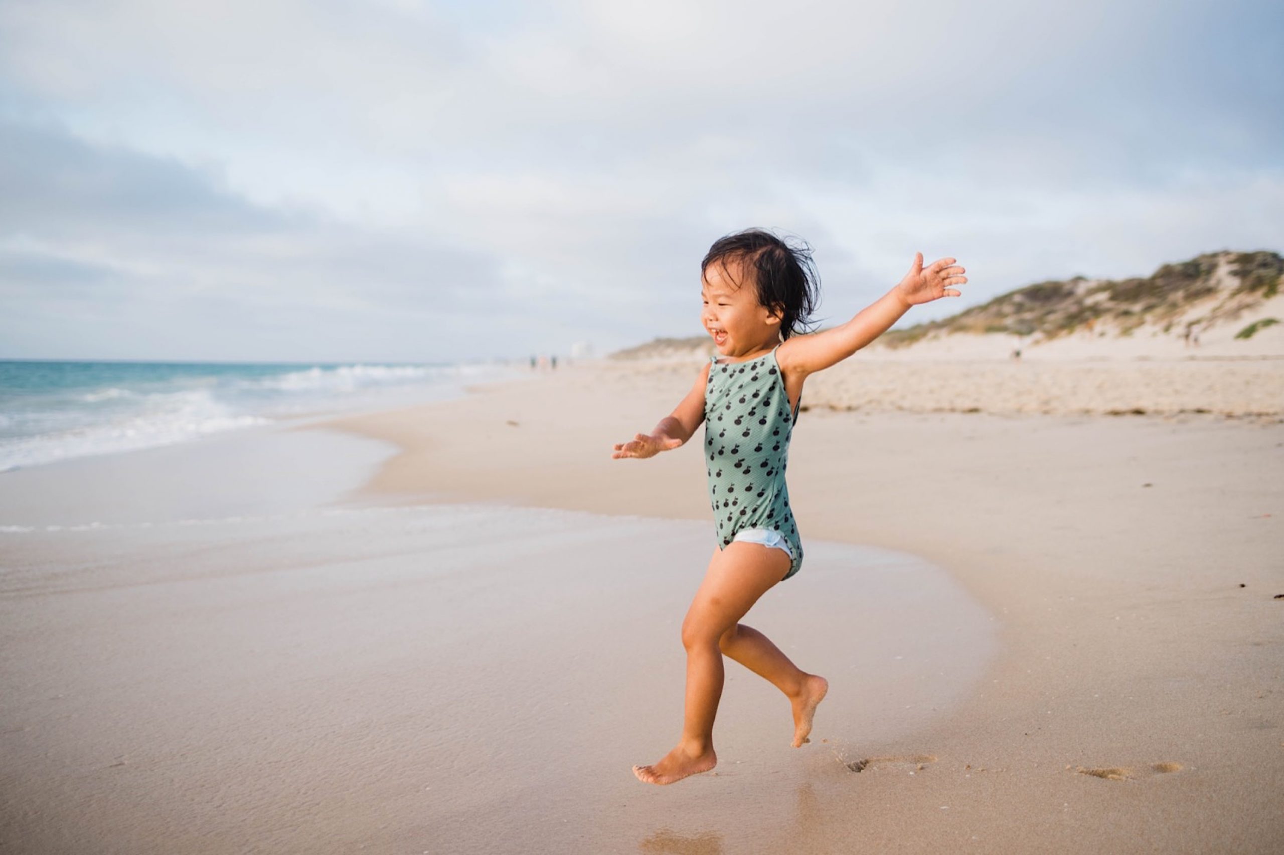 A child leaps through the air running towards the ocean at Floreat Beach.