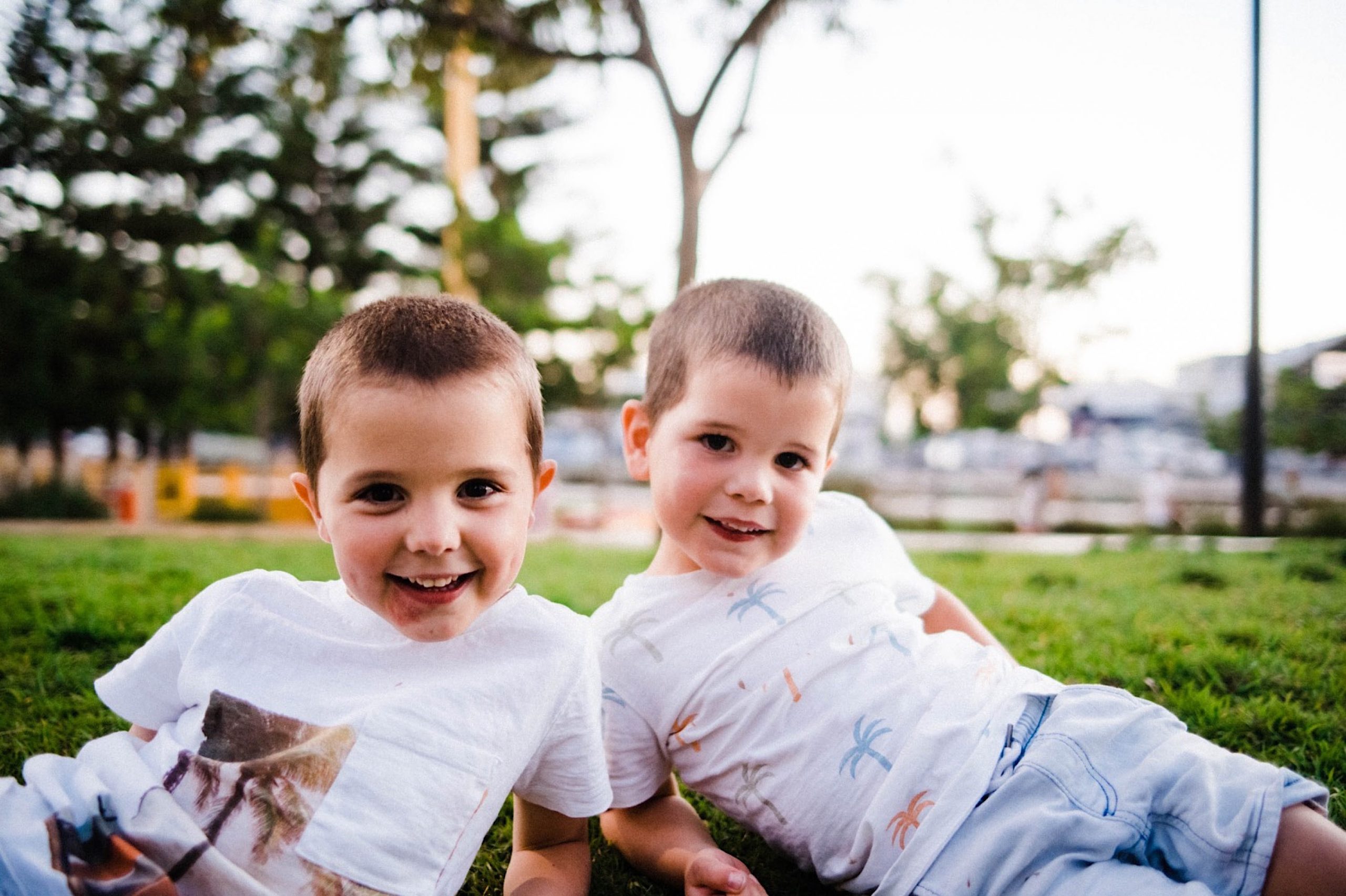 Two brothers, lie on a grassy hill at the Fremantle Esplanade Park, smiling at the camera. 
