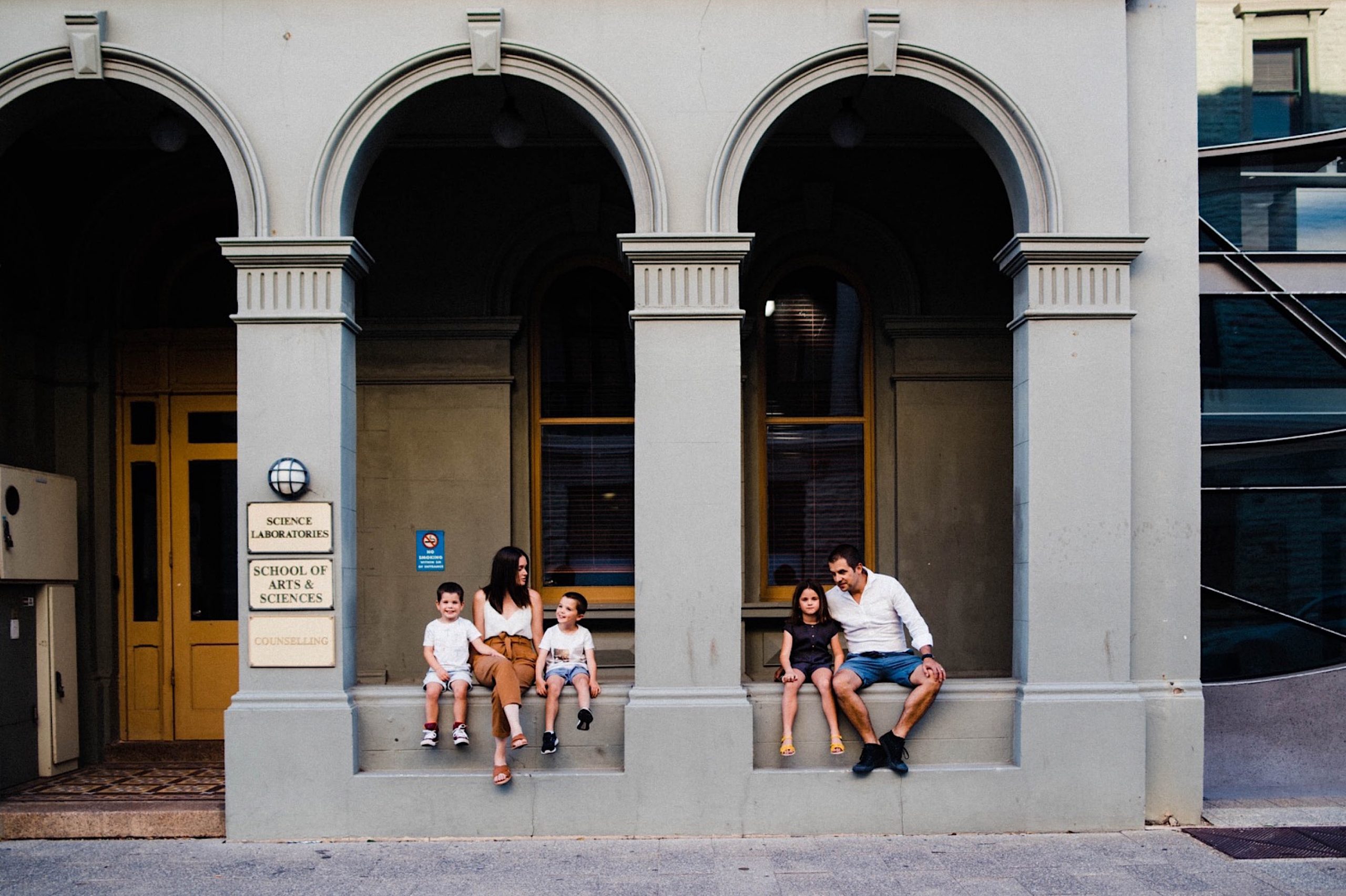 A portrait of a family of five, sitting in the archways of an old building in Fremantle, the two boys sitting with their Mum on the left side, and the girl sits with her Dad on the right.