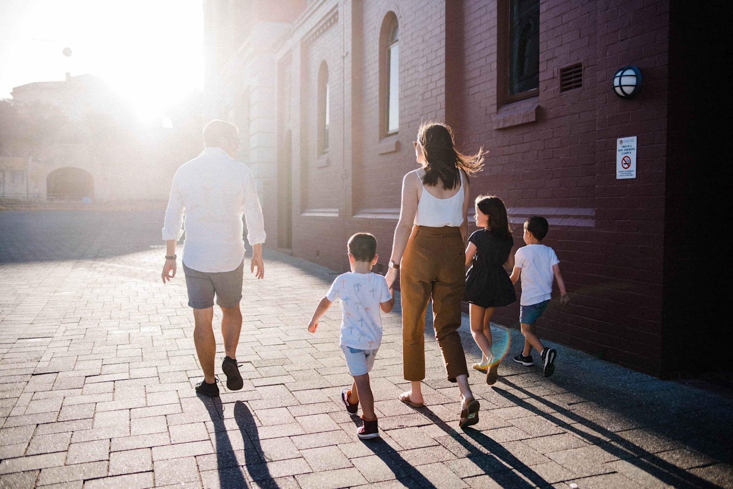 A candid portrait taken in Fremantle of a family walking towards a setting sun, with heritage buildings in the background. 