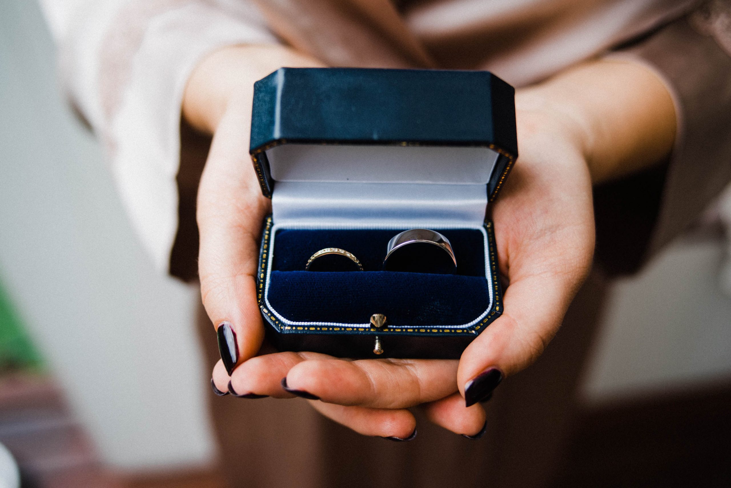 A bride holds her wedding rings, made sustainably by Digby and Iona, in her hand in a blue jewellery box.