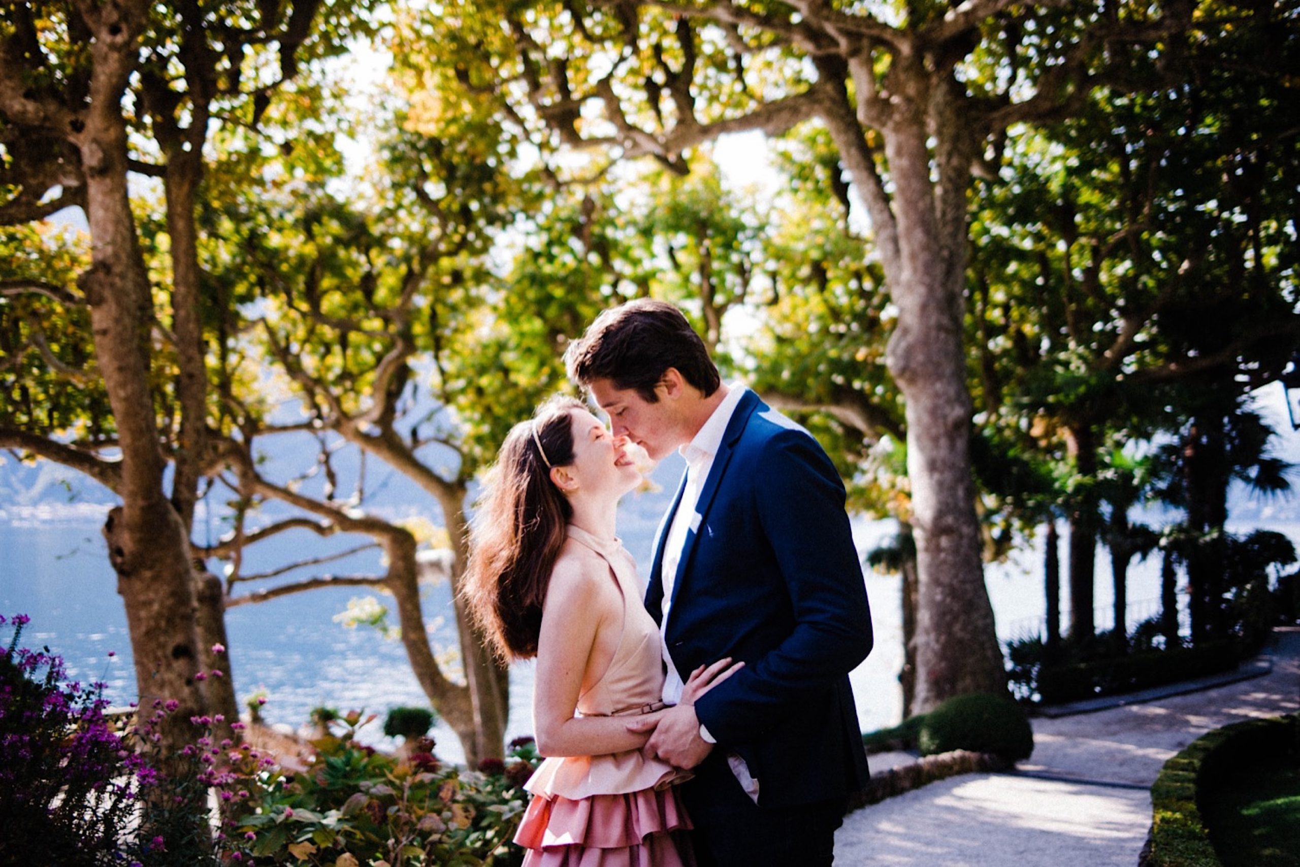 A mid-shot of a newly engaged couple kissing each other in front of gardens by Lake Como, in Northern Italy.