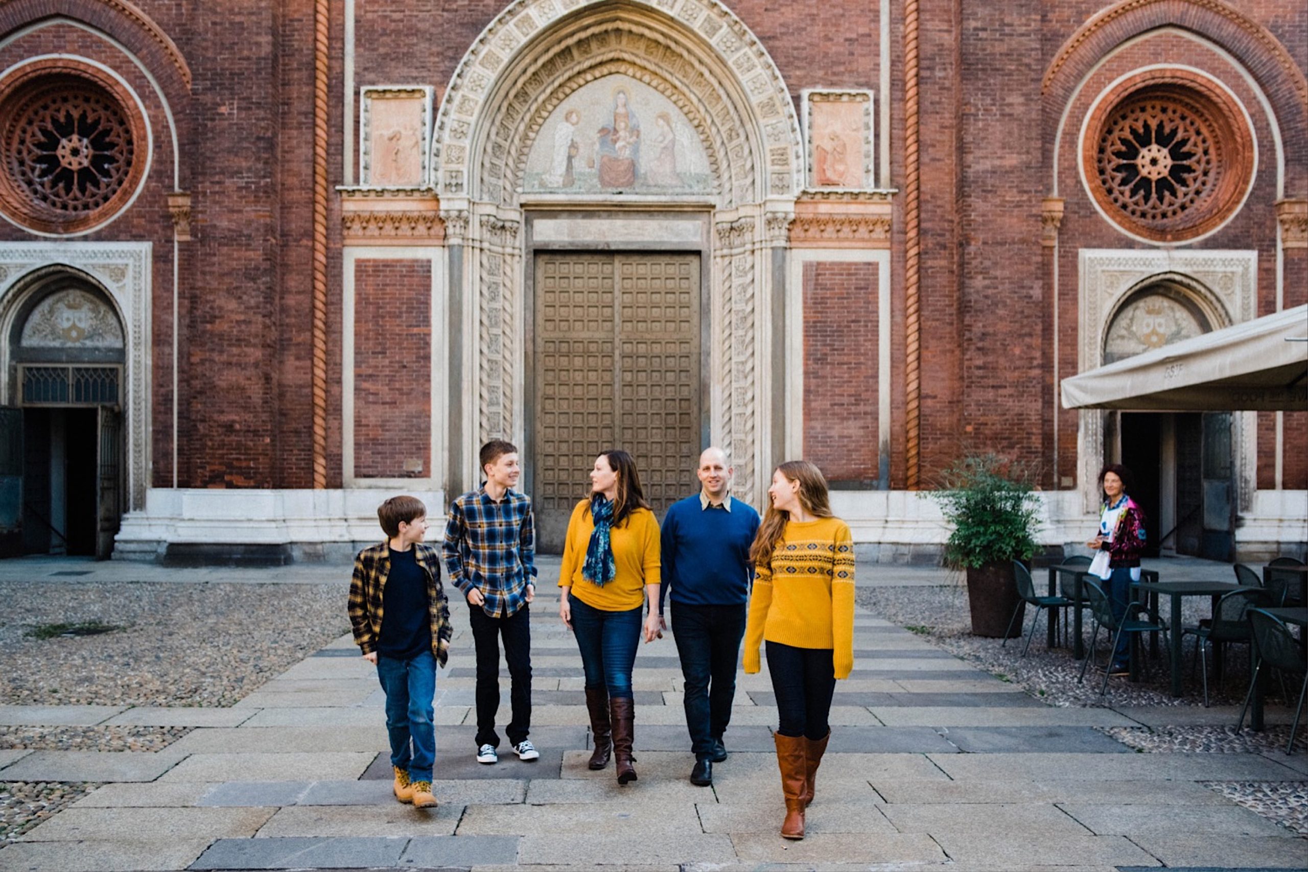 A wide photo of a family walking in front of one of Milan's Chiesa del Carmine.