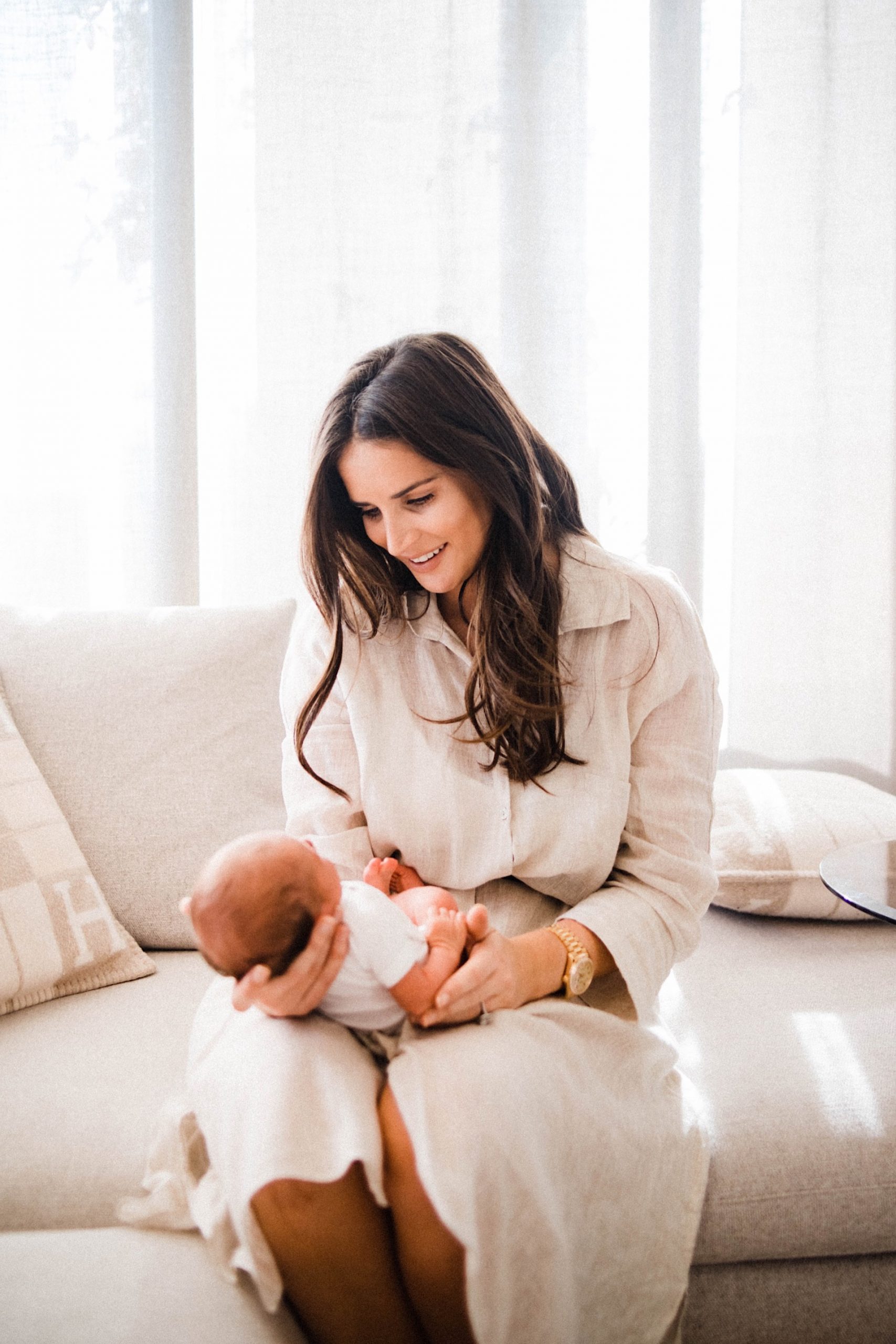 Mid-shot portrait photo of new Mum, Erin Borini, wearing a blush linen shirt dress smiling at her newborn who she's holding on her lap during their Italian Newborn Photography session.