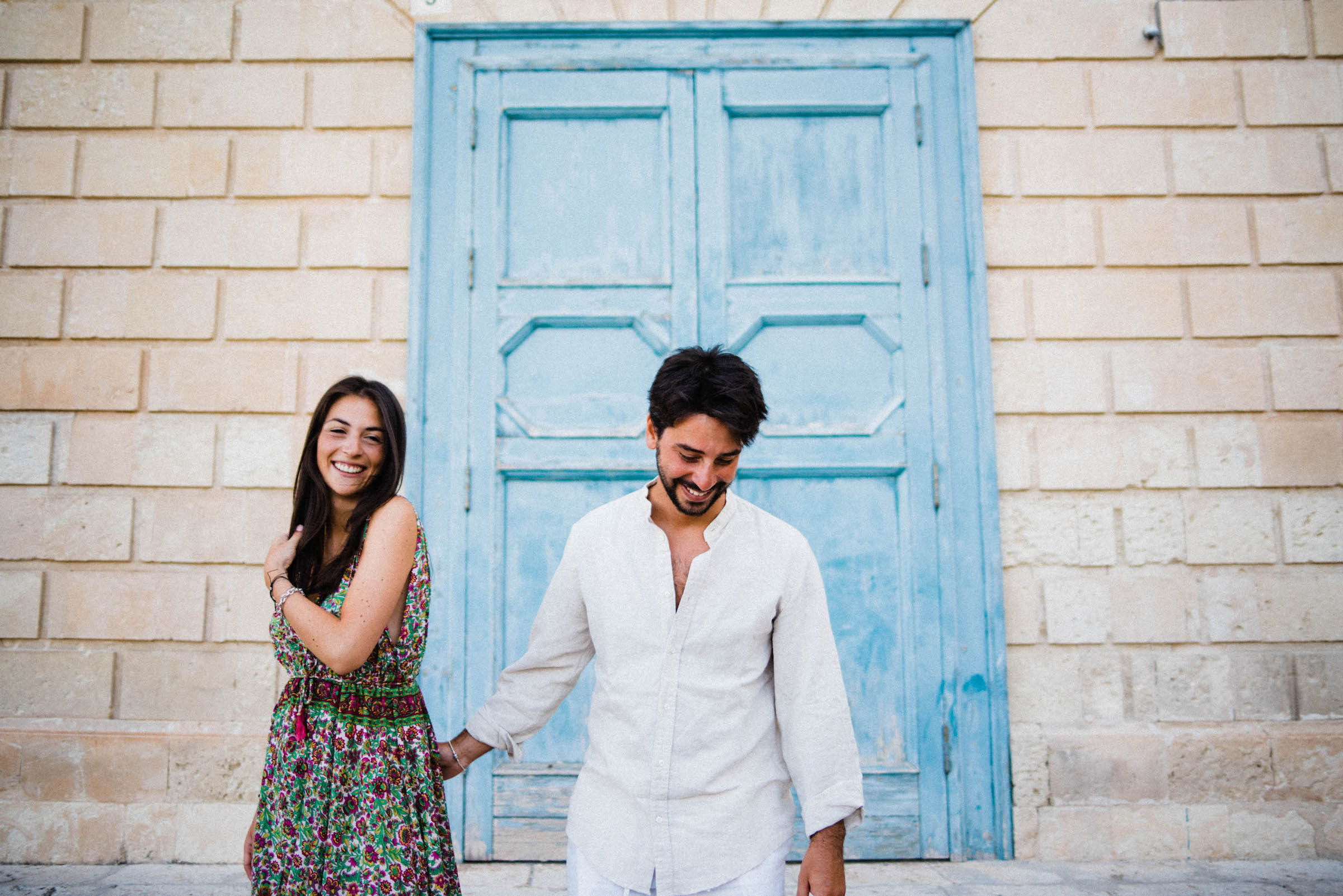 Italian Wedding Photographer's work of a couple during their Sicily Couples Photography session at Noto, standing in front of a blue door and laughing.