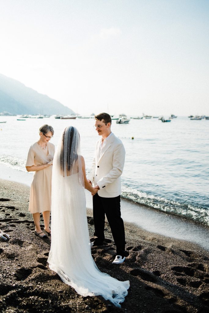 A wide shot of a couple during their Fornillo wedding ceremony, with the beach and the sky taking up most of the frame, showing How to Elope in Positano.