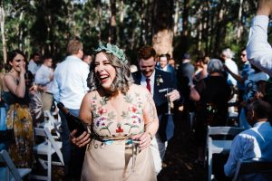 Mid-shot of a smiling bride & groom walking back up the aisle with a bottle of prosecco taken by Perth Wedding Photographer